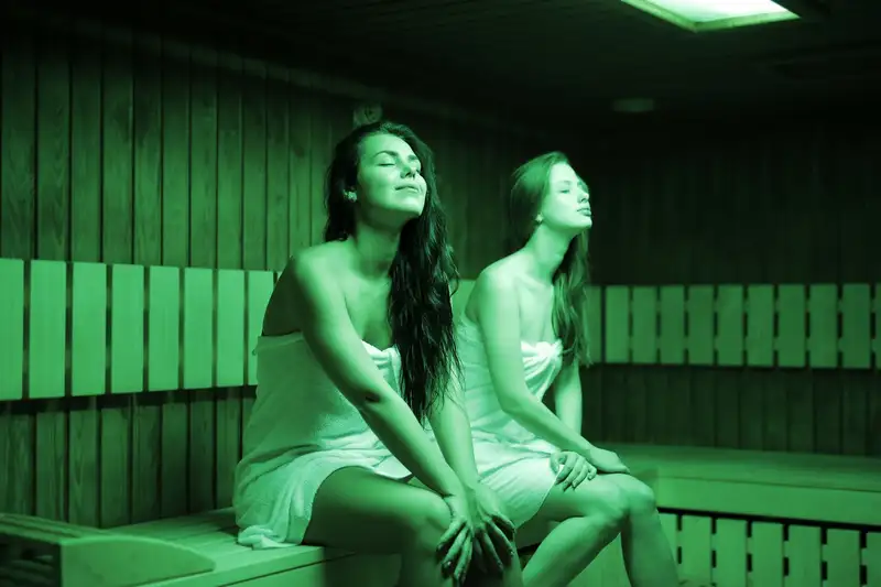 Two women in a sauna, wrapped in towels, enjoying relaxation and warmth indoors.