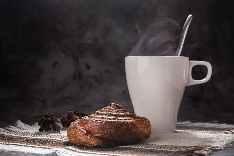 A cinnamon pastry and steaming mug on a rustic cloth. Ideal for breakfast scenes.