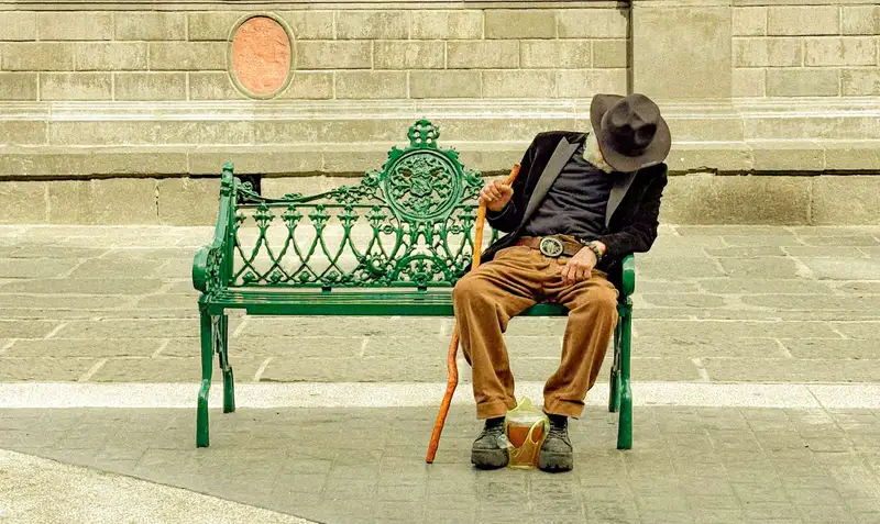An elderly man in a hat resting on a park bench in Puebla, Mexico.